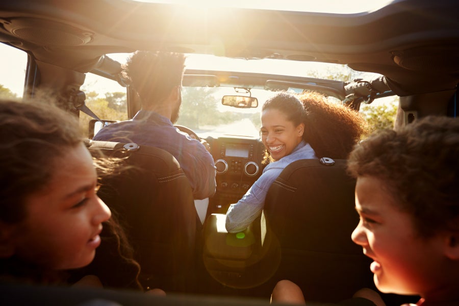 A family of four on a sunny road trip in a convertible, viewed from the back seat.